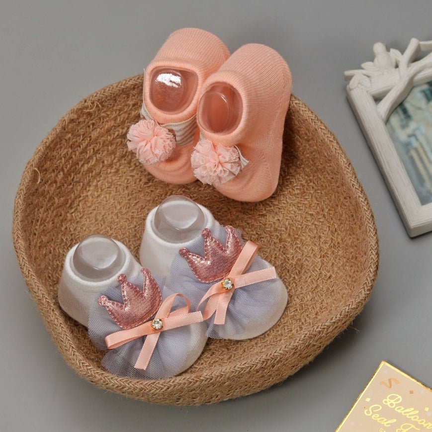 Peachy pink baby socks with pom-poms and a straw hat display.