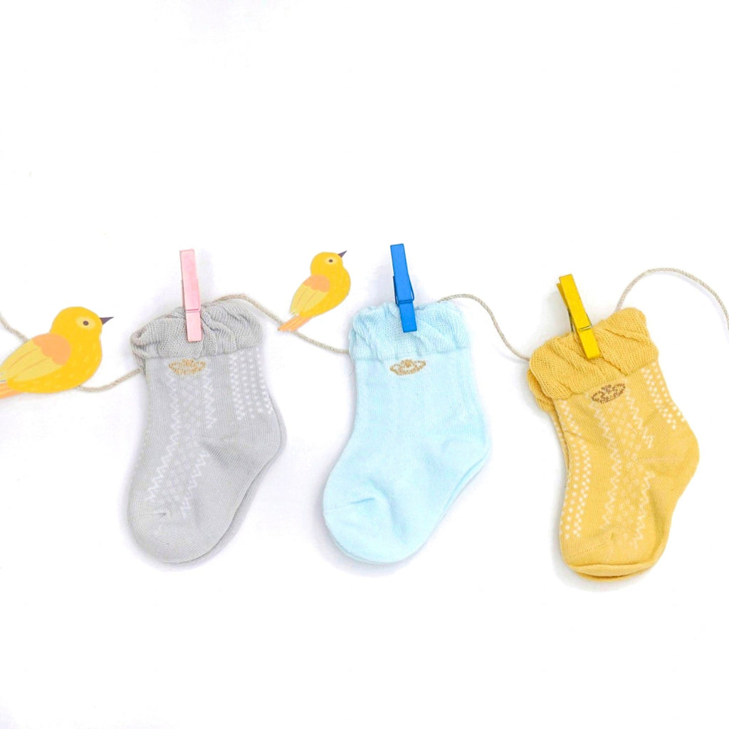 Pastel-colored baby girl socks with crown accents hanging on a line.