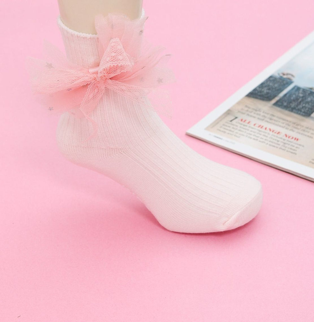 A child wearing a pink sock with a fluffy tulle bow on a soft pink background.