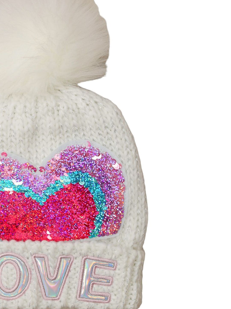 Close-up of a girls' white beanie highlighting the reversible sequin heart and pom-pom detail.