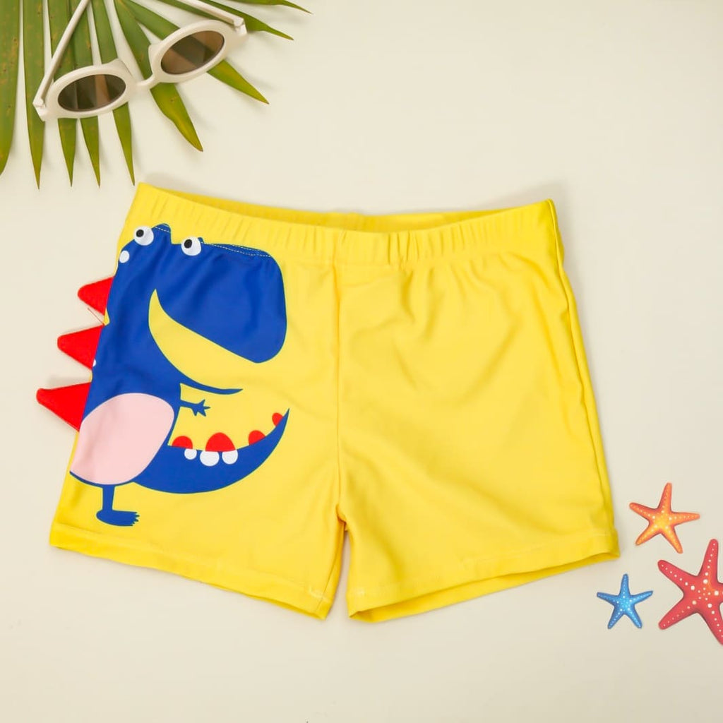 Flat lay of yellow dino swim shorts for boys with a blue dinosaur print and red fin