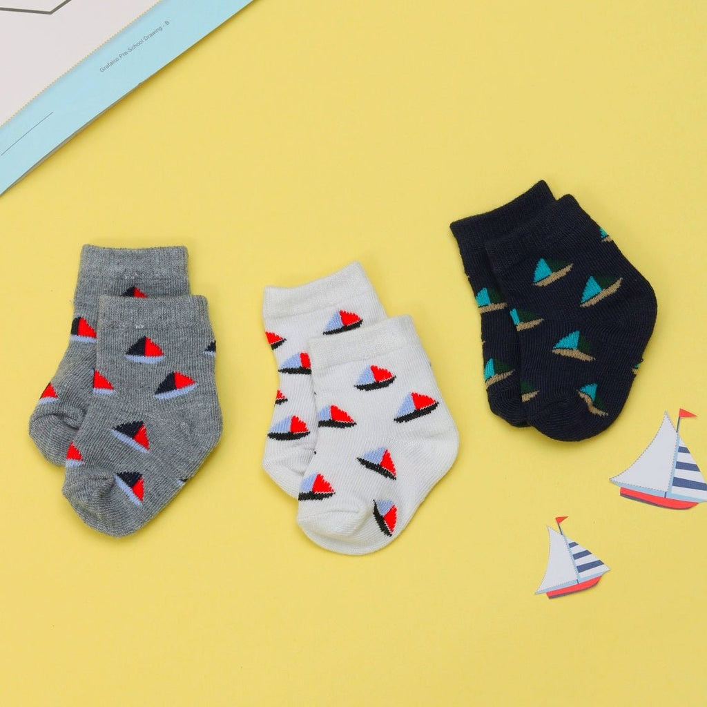 Grey, white, and navy baby boy socks with colorful boat prints on yellow background