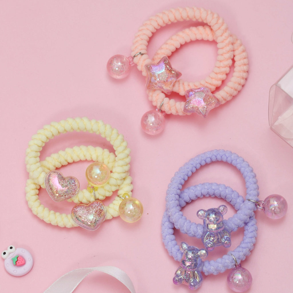 A delightful arrangement of Yellow Bee's soft braided hair ties with heart and star pendants on a pink surface.
