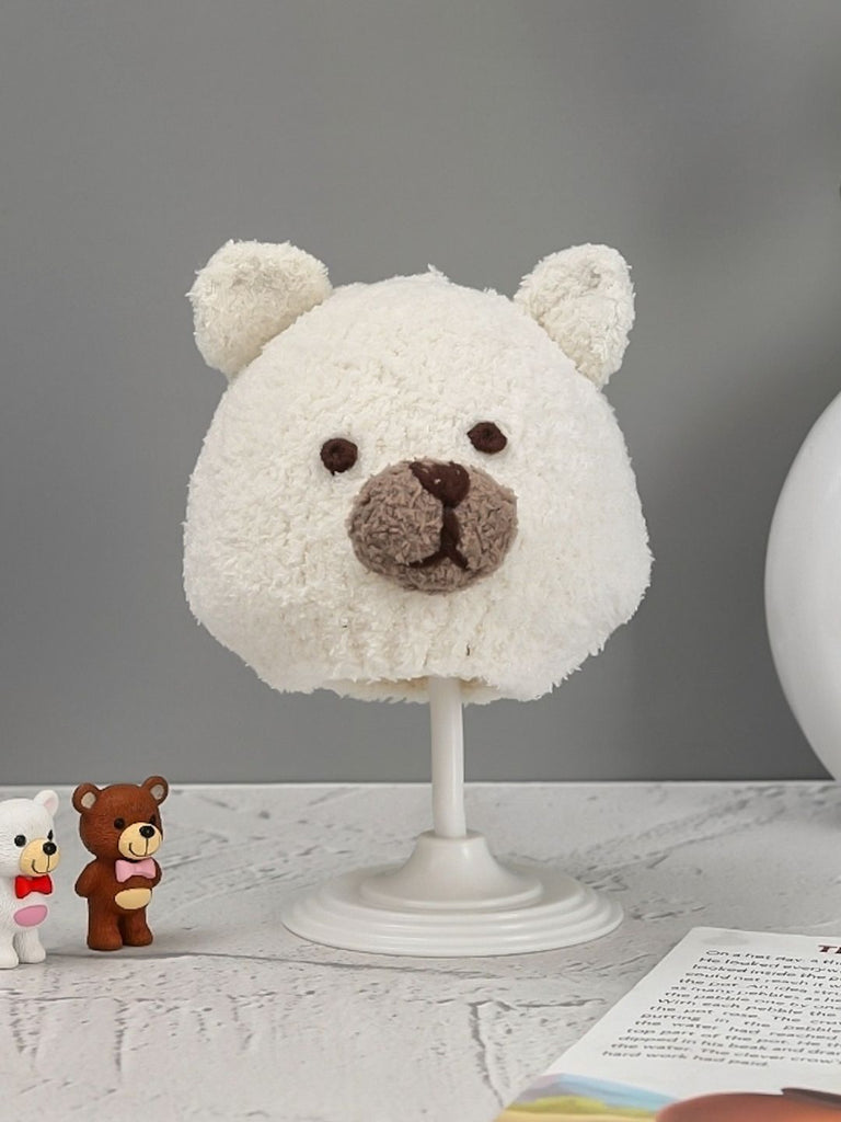 Adorable white bear-themed knitted beanie for boys with ear accents, presented on a display stand.