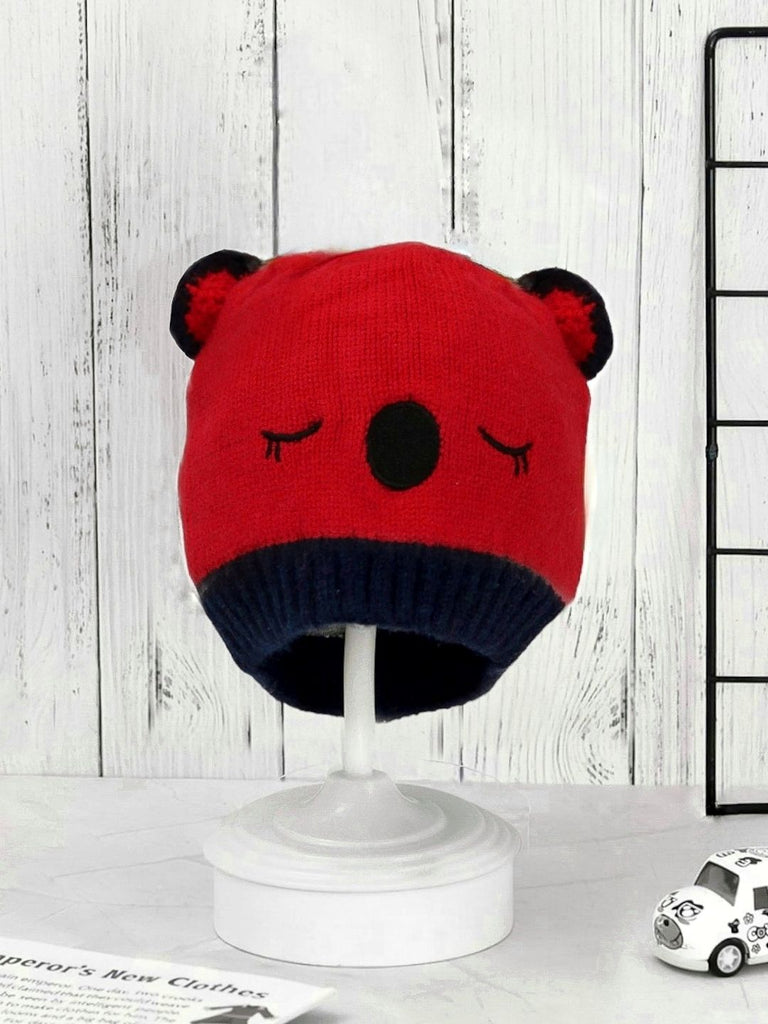 Red knitted beanie with teddy ears and navy band for boys on a display stand.