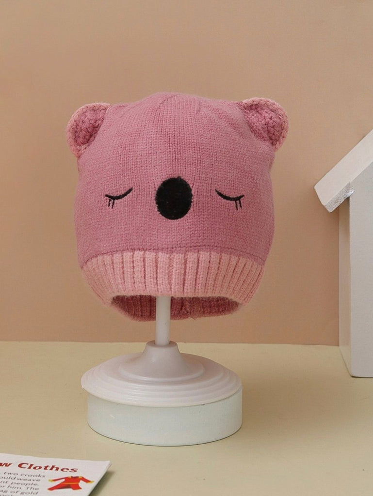 Dark pink knitted beanie with teddy ears for girls displayed on a stand.