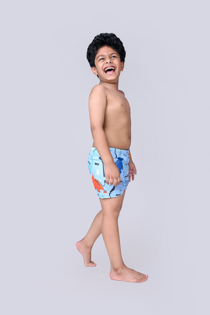 Joyful young boy laughing in blue dinosaur print swim shorts, ready for summer fun.