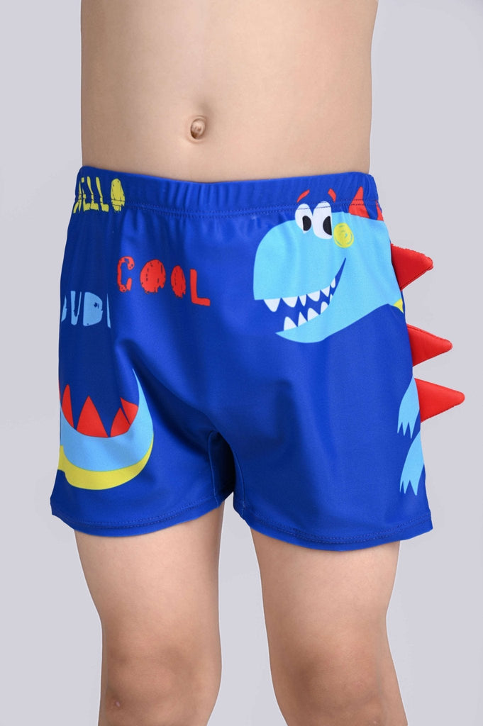 Close-up view of a child wearing blue dino swim shorts with red fin accents and playful lettering