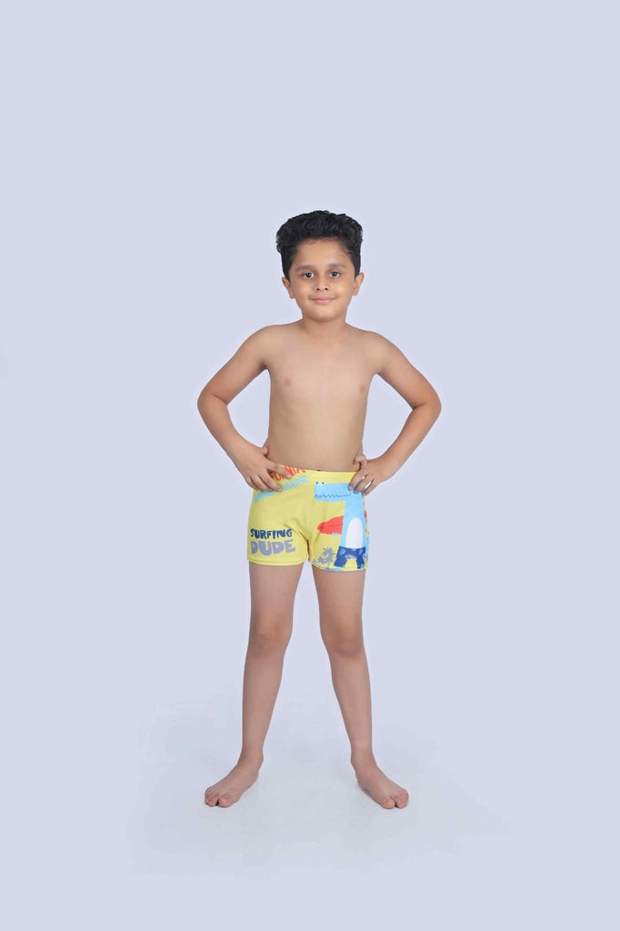 Young boy smiling and posing in yellow crocodile swim shorts, ready for fun in the sun and surf lessons.