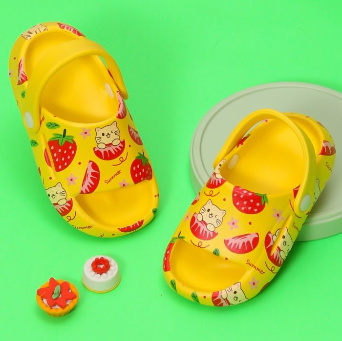 Vibrant yellow kids' sandals with strawberry and cat print on a green background