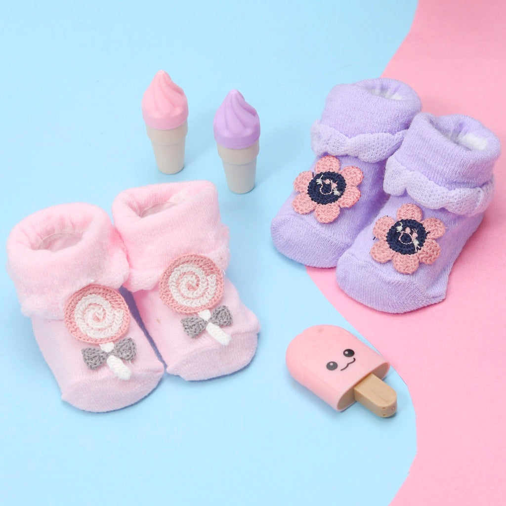Soft pink and lavender baby socks with candy swirls and crochet flower accents alongside toy ice cream cones.