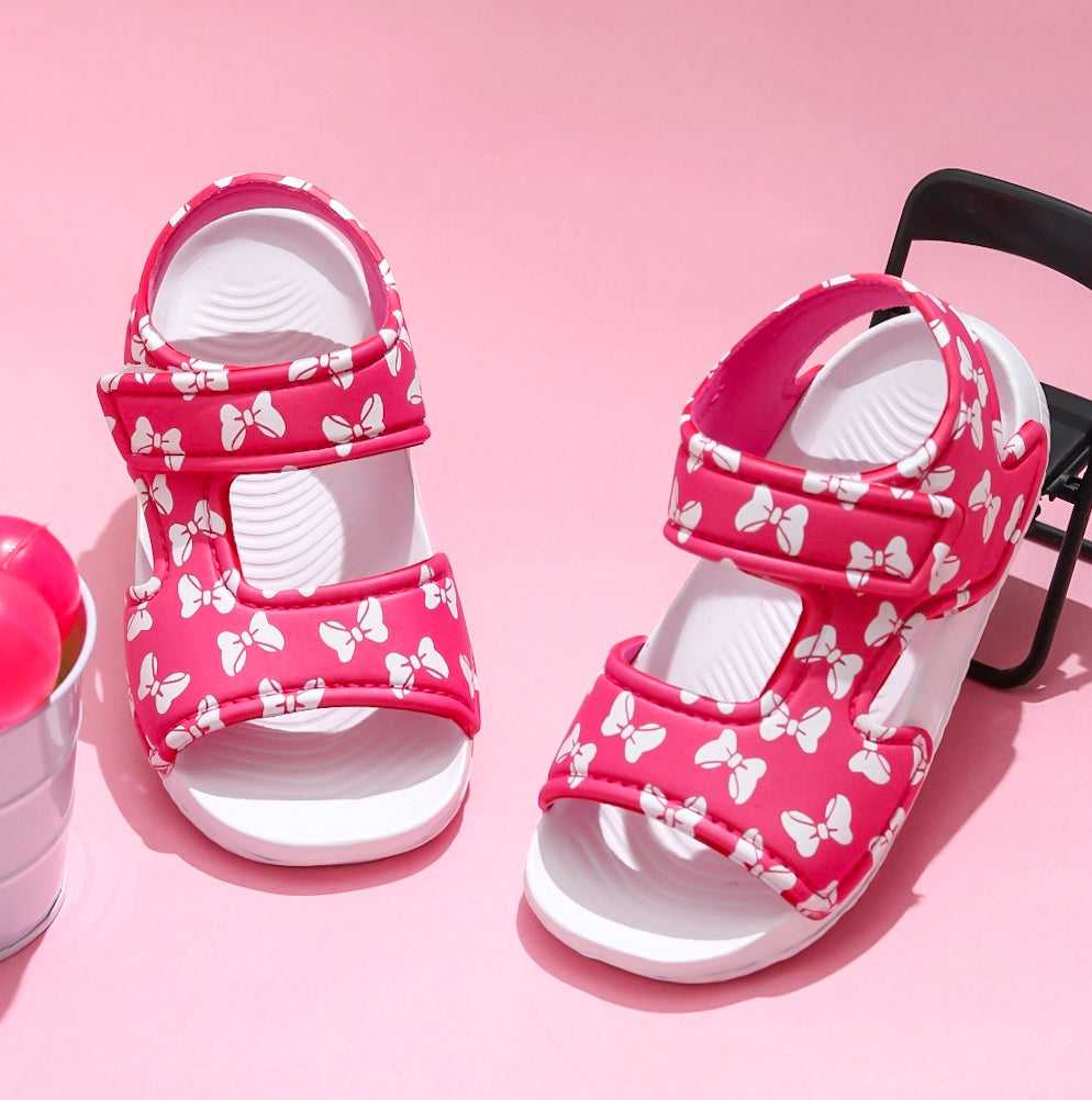 Pair of pink sandals with white bow print for children on a stylish background