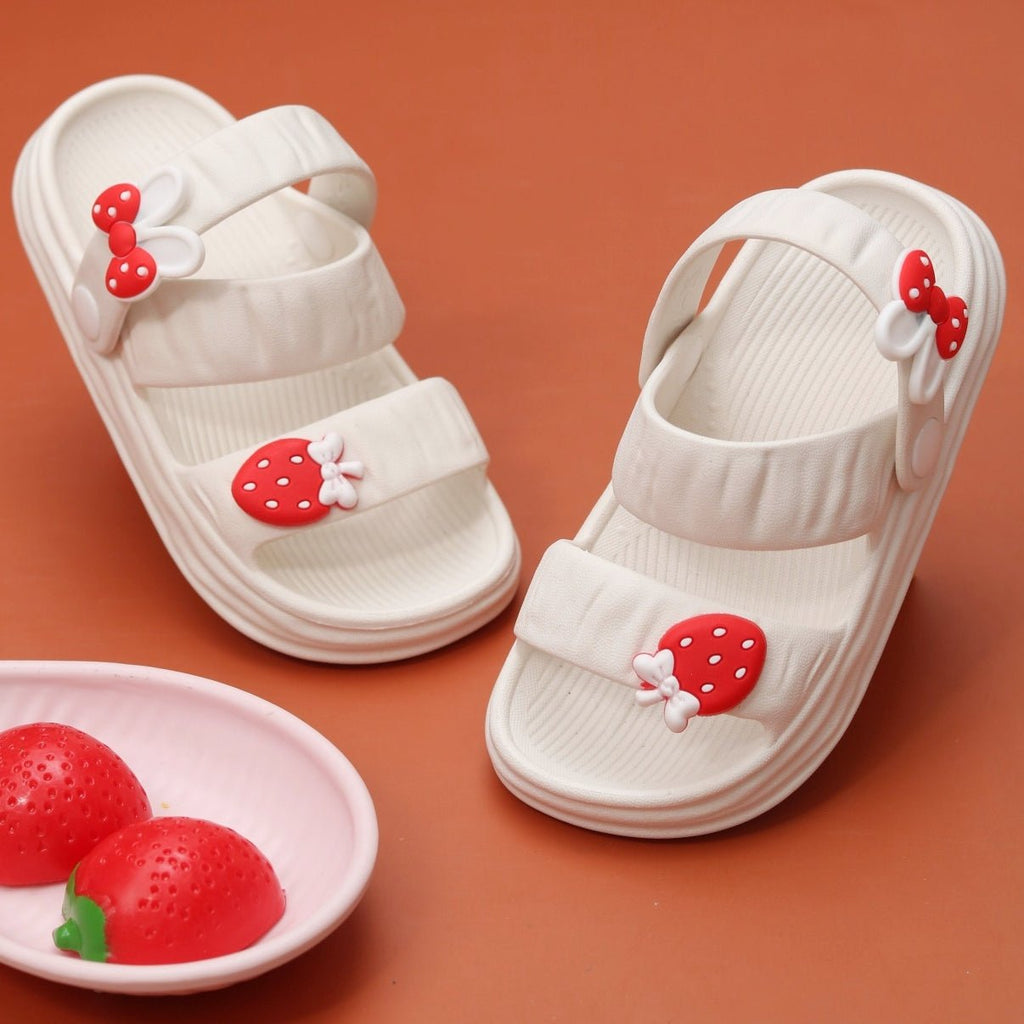 Kids' white sandals with strawberry and bow decorations on a warm terracotta background.