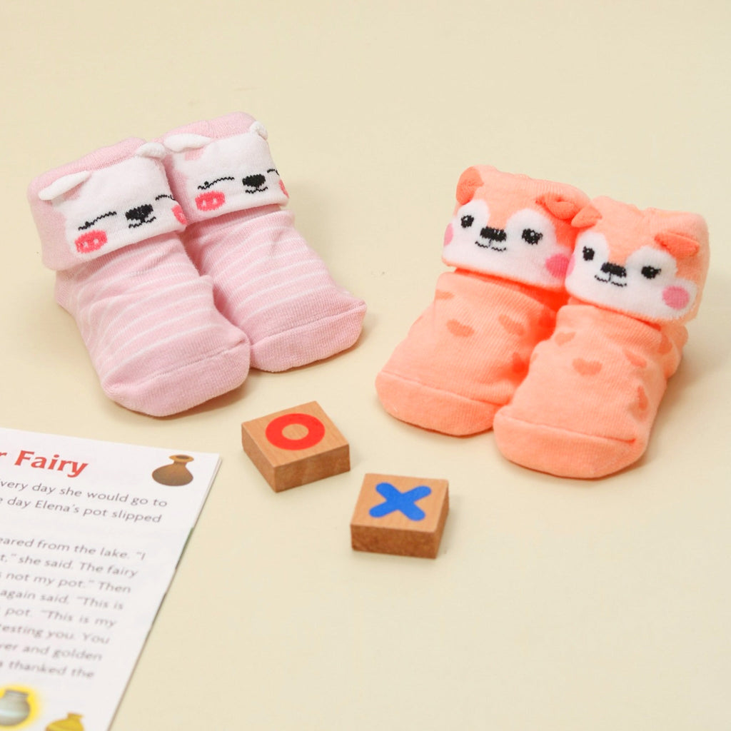 Assortment of Yellow Bee's animal-themed anti-skid baby socks in pink hues, displayed with wooden toy blocks on a beige background.