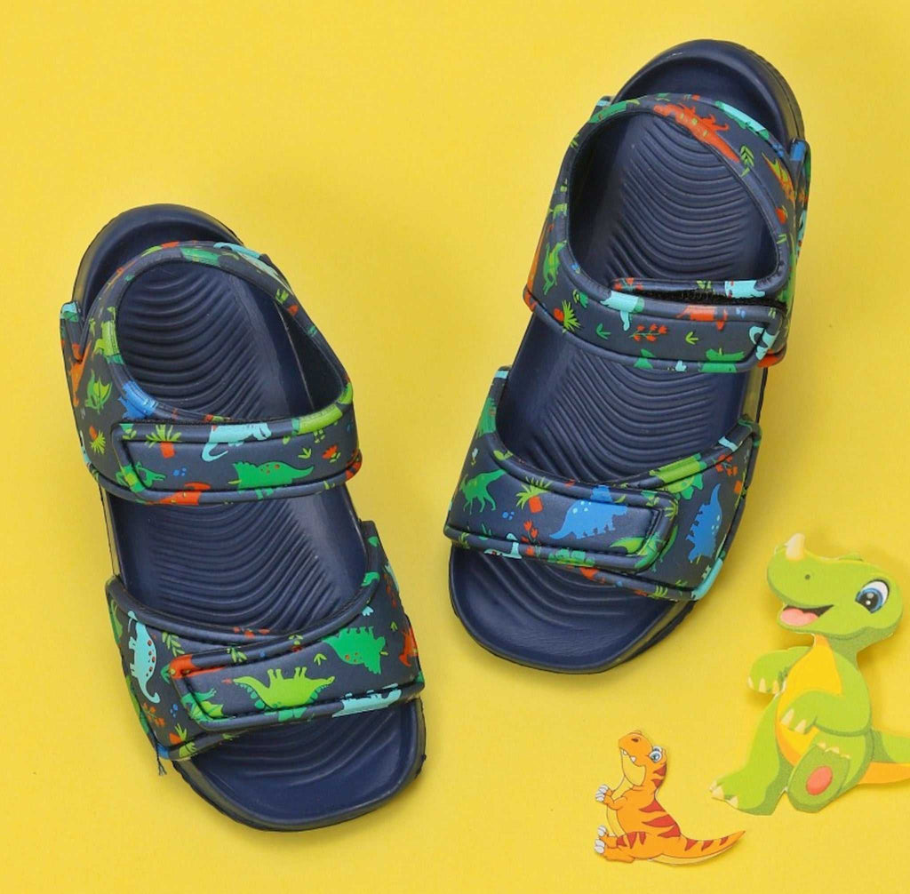 Pair of navy-colored kids' sandals with an all-over dinosaur print, set against a sunny yellow background.